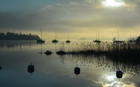 Calm, winter light on Derwent Water with silhouetted sailing boats